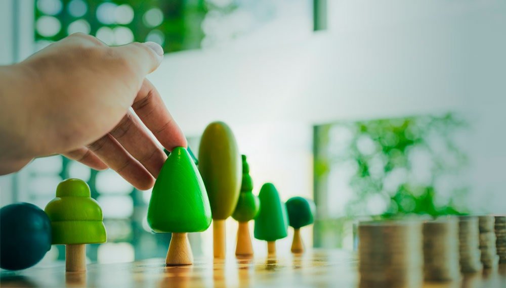 Mano acomodando figuras en forma de árbol y monedas ordenadas sobre una mesa.